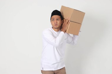 Karton taşımakta zorlanan Koko gömlekli yorgun Asyalı Müslüman adamın portresi. Bayram için eve gidiyorum. Beyaz arkaplanda izole edilmiş resim