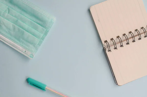 Mavi arka planda kalem ve tıbbi maskeli bir defter. Üst Manzara. Boşluğu kopyala