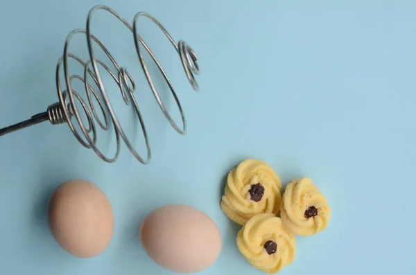 Tavuk yumurtalı pasta ve mavi arka planda elle yumurta çırpıcı.