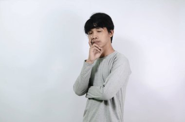 Asyalı adamlar gri uzun kollu tişörtler giyiyorlar. Üzgün ve kafası karışmış genç bir adam.