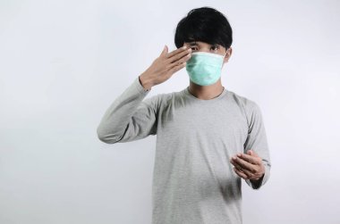 Asyalı erkeklerin başı dönüyor. Gri tişörtlü ve beyaz arka planda izole edilmiş tıbbi maske takan Asyalı bir adam.