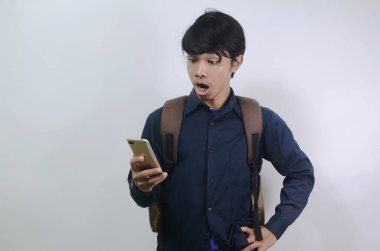 Mavi gömlek giyen ve beyaz arka planda izole edilmiş çantalar taşıyan Asyalı genç adamlar. Cep telefonunun ekranını görünce şok olan genç adamın ifadesi.