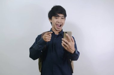 Mavi gömlek giyen ve beyaz arka planda izole edilmiş çantalar taşıyan Asyalı genç adamlar. Cep telefonunun ekranını görünce şok olan genç adamın ifadesi.