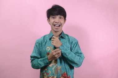 Mutlu görünen genç Asyalı erkeklerin portresi. Pembe arka planda izole edilmiş batik gömlek giyen Asyalı genç bir adamın portresi.