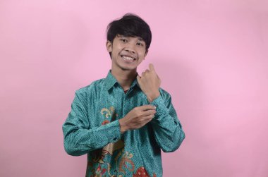 Mutlu görünen genç Asyalı erkeklerin portresi. Pembe arka planda izole edilmiş batik gömlek giyen Asyalı genç bir adamın portresi.