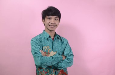 Mutlu görünen genç Asyalı erkeklerin portresi. Pembe arka planda izole edilmiş batik gömlek giyen Asyalı genç bir adamın portresi.