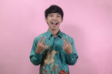 Mutlu görünen genç Asyalı erkeklerin portresi. Pembe arka planda izole edilmiş batik gömlek giyen Asyalı genç bir adamın portresi.