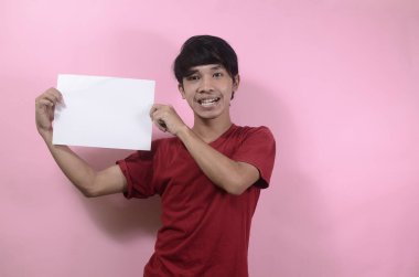 Genç adam yazı ve metin için boş bir poster tutuyor. Kırmızı tişört giyen Asyalı adamlar pembe arka planda izole edilmiş.