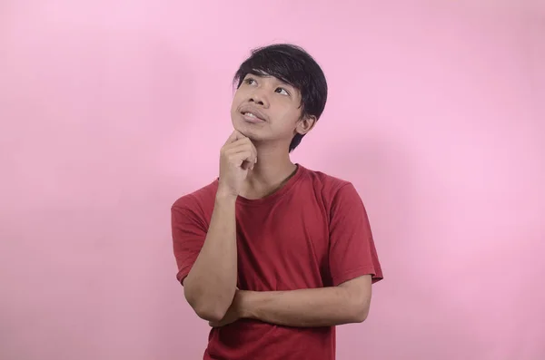 男達は見上げながら考え事をしている ピンクの背景に赤いTシャツを着たアジア系男性 — ストック写真