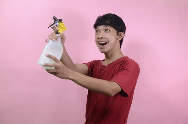 Man with water sprayer in hand. Asian men wearing red t shirts isolated on a pink background