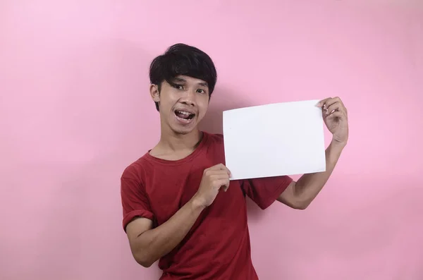 少年は文章を書くための空白のポスターを持っている ピンクの背景に赤いTシャツを着たアジア系男性 — ストック写真