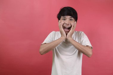 Mutlu Asyalı adamın şaşırmış yüzü. Kırmızı arka planda beyaz tişörtler giyen Asyalı adamlar.