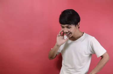 Aşağıya bakan ve mutlu görünen bir adam. Kırmızı arka planda beyaz tişörtler giyen Asyalı adamlar.