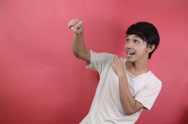 İfadesi olan bir adam vurmak ister. Kırmızı arka planda beyaz tişörtler giyen Asyalı adamlar.