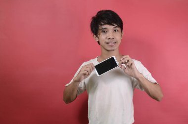 Mutlu gülümseyen Asyalı genç adam cep telefonunu gösteriyor. Kırmızı arka planda beyaz tişörtler giyen Asyalı adamlar.