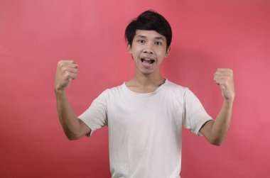 Kazanan bir jest yapan mutlu ve hevesli bir gencin portresi. Kırmızı arka planda beyaz tişörtler giyen Asyalı adamlar.