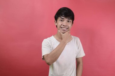 Genç adam mutlu görünüyor. Kırmızı arka planda beyaz tişörtler giyen Asyalı adamlar.