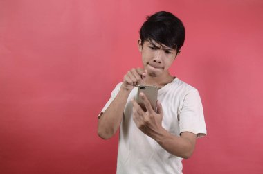 Asyalı bir adamın yüzü akıllı telefonda gördüklerine şaşırır. Kırmızı arka planda beyaz tişörtler giyen Asyalı adamlar.