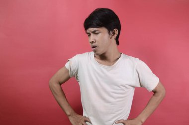 İfadesini bozan genç bir adam. Kırmızı arka planda beyaz tişörtler giyen Asyalı adamlar.