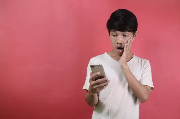 Asyalı bir adamın yüzü akıllı telefonda gördüklerine şaşırır. Kırmızı arka planda beyaz tişörtler giyen Asyalı adamlar.