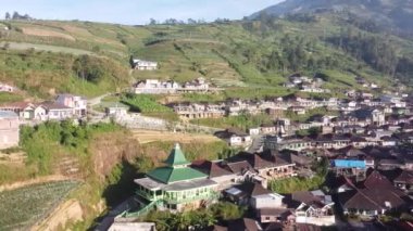 Bir dağın yamaçlarında düzgünce dizilmiş evleri olan bir köy.