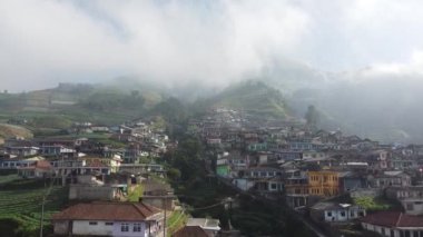 Bir dağın yamaçlarında düzgünce dizilmiş evleri olan bir köy.