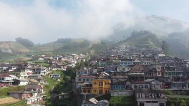 Bir dağın yamaçlarında düzgünce dizilmiş evleri olan bir köy.