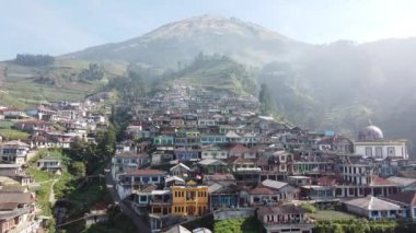 Bir dağın yamaçlarında düzgünce dizilmiş evleri olan bir köy.