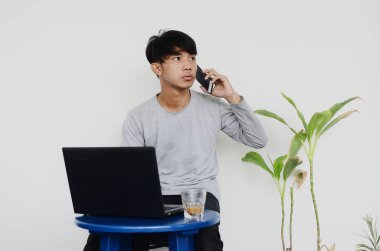 Asyalı genç adam dizüstü bilgisayarın önünde oturuyor ve şaşkın bir suratla arıyor.