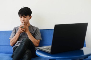 Asyalı adam kanepede sigara içiyor.