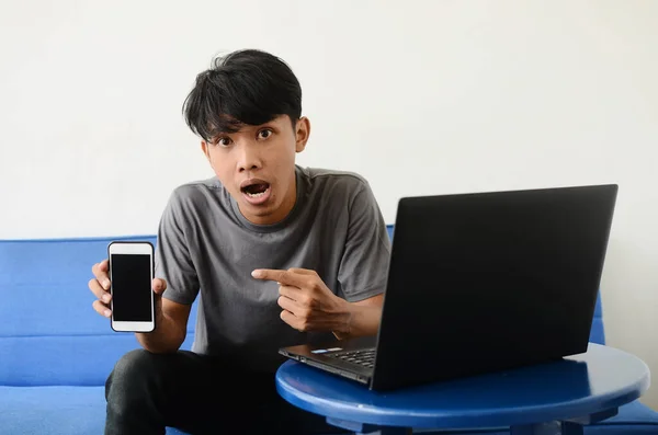 Asijský Mládež Sedí Pohovce Před Notebookem Ukazuje Svůj Mobil — Stock fotografie