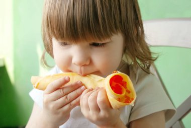 Küçük bir kız ellerini tutuyor ve kırmızı havyarlı kızarmış gözleme yiyor. Çocuk evde yiyor.