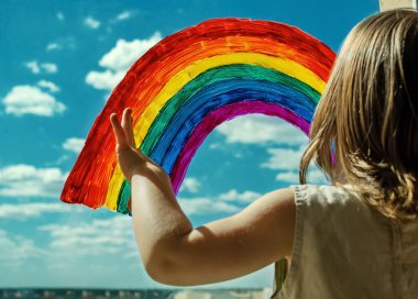 Küçük bir kız pencerenin kenarında duruyor ve parmağıyla penceredeki parlak renkli gökkuşağını işaret ediyor. Bulutlu güzel bir gökyüzü. Mutluluğun sembolü