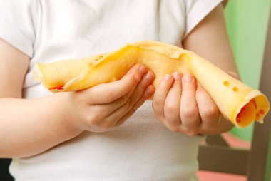 Küçük bir çocuk havyarlı sarı bir krep tutuyor. Çocuk mutfakta yemek yiyor.