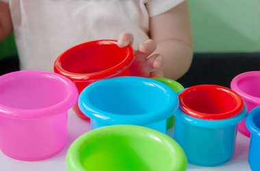 Bir çocuk yeşil, mavi ve kırmızı bardaklarla plastik oyuncaklarla oynar