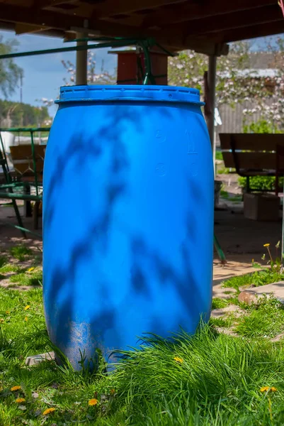 blue plastic barrel for draining rainwater from sewer pipes on green grass in summer. Large water storage barrel