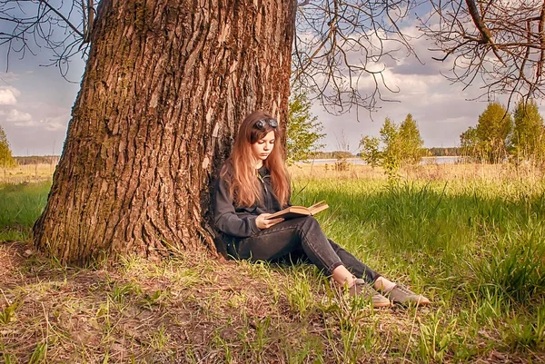 Piękna Młoda Dziewczyna Siedzi Przyrodzie Pod Dużym Drzewem Czyta Książkę — Zdjęcie stockowe
