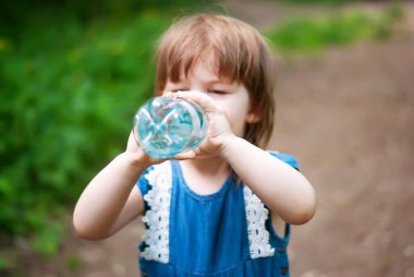 Güneşli bir günde, dışarıda bir tarlada, plastik şişeden su içen güzel bir kız. Çocuk su içiyor.