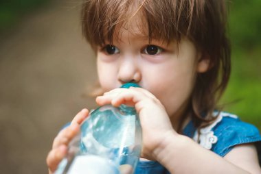 Güneşli bir günde güzel bir kız plastik şişeden su içer. Çocuk saf maden suyu içiyor.
