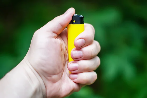 Caddenin dışındayken bir kadının eli çakmağı tutuyor. Bir kadının elinde sarı bir çakmak.