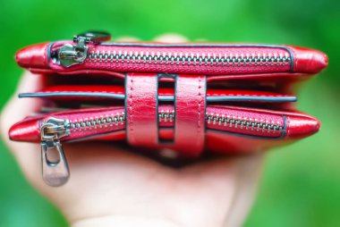 Kırmızı, güzel kadın deri cüzdanı, yeşil yaprakların bulanık arka planında.