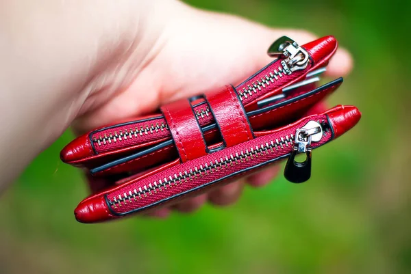 Kırmızı kadın deri cüzdanı yeşil yaprakların bulanık arka planında.