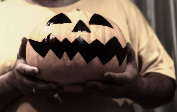 An unrecognizable blurry man holds Jack's Halloween pumpkin in front of him with a gruesome drawn face close-up. Evil smiling pumpkin in hands