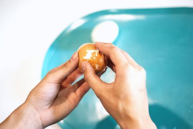 Kadınların elleri mutfakta haşlanmış bir yumurtayı temizler. Yumurta temizleme işlemi. Genç bir kadın kahvaltı hazırlıyor. Sağlıklı yemek. Keto diyeti.