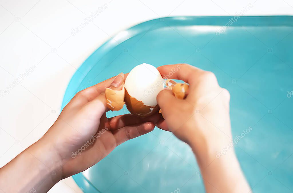 Women's hands clean a boiled egg in the kitchen. The process of cleaning eggs. A young woman is preparing Breakfast. Health food. Keto diet. Cleaning the egg from the shell