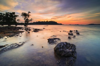 Batam Adası 'nın Tanjung Pinggir sahilinde gün batımı, sahil boyunca kayalar.