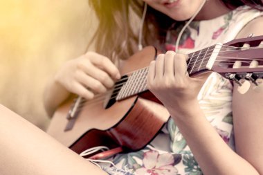 Parkta akustik gitar çalan Asyalı genç bir kadın. Renk tonuyla.