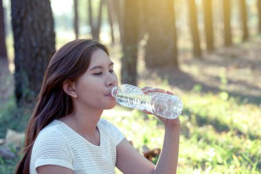 Asyalı genç bir kadın doğa parkında su içiyor. Renk tonuyla.