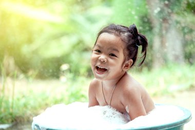 Mutlu Asyalı küçük kız banyo yapıp köpükle oynuyor.