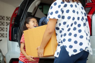 Mutlu Asyalı kız ve anne taşınma günü taşınmak için arabaya birlikte taşınan eşyalarla dolu bir karton kutuyu taşımaya yardım ediyor. Ev yenileme ve taşınma konsepti.